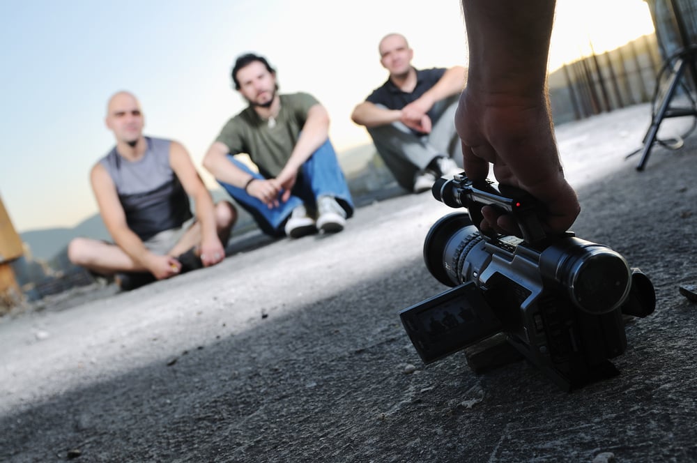 three young man siting on ground while modern video camera recording three young man siting on ground while modern video camera recording